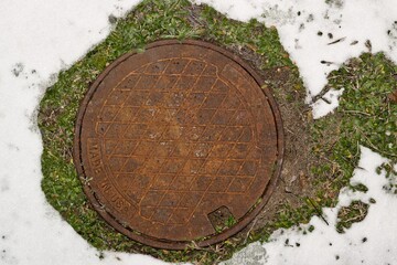 Rusty manhole cover in Winter snow directly above industrial made in usa label.