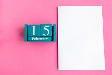 February 15. Blue cube calendar with month and date and white mockup blank on pink background.