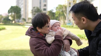 A 6 -month -old baby, Shanghai, China, and grandmother live. They stand in a warm winter dress in the lawn park between apartments