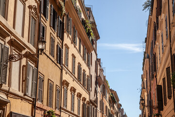 Fototapeta premium Sunlit building facades in Old Rome (Italy) display classic shutters and pastel walls, revealing the city’s real estate character. These historic properties underscore the area’s timeless allure.
