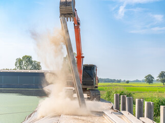 The backhoe is lifting the pile, with dust spreading around.