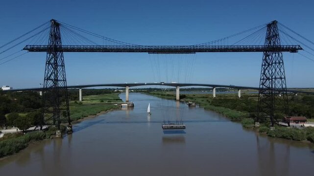 Aerial approach to the transporter bridge in Rochefort sur Mer, France. Suspended platform crossing the river and sailboat in the background.