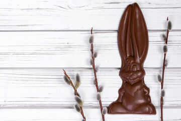Flat lay of Easter decor on a wooden rustic white table with chocolate big bunny and branches of pussy willow.