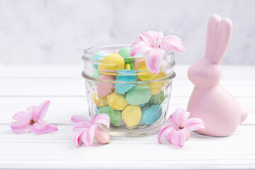 Easter decor on the white wooden table with ceramic pink bunny, colorful chocolate eggs in a glass jar and hyacinth pink flowers around.