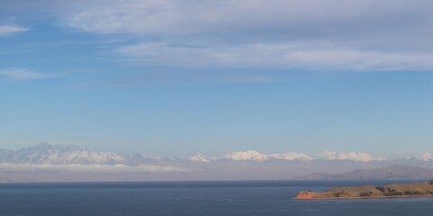 A serene rural landscape overlooking lake Titicaca, the image features a clear blue sky with scattered clouds, natural vegetation, and a peaceful ambiance 