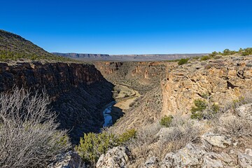 Obraz premium Panoramic view of a deep canyon with a winding river, surrounded by rocky cliffs and sparse vegetation