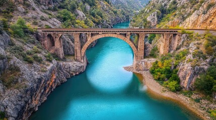 Fototapeta premium Overhead shot of a railway bridge crossing a calm river, vibrant natural surroundings and clear blue water below