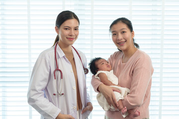 Smiling pediatrician posing with cheerful mother holding newborn baby in clinic. Scene emphasizes...