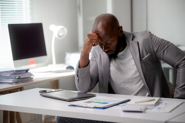 Stressed professional experiencing headache while reviewing paperwork at cluttered workspace