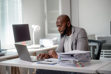 Fototapeta premium Concentrated manager typing on his laptop, surrounded by paperwork in a bright, contemporary office