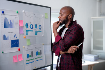 Thoughtful african american manager contemplates data displayed on charts and graphs, strategizing for business success