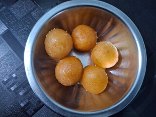 Soft, golden-brown gulab jamuns soak in fragrant sugar syrup, served in a gleaming stainless steel bowl, tempting with their rich, melt-in-mouth sweetness.