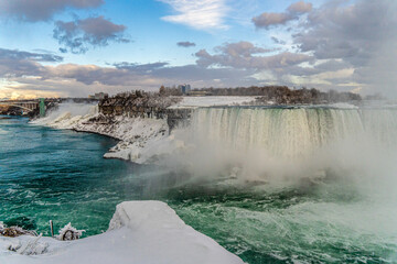A breathtaking winter scene of Niagara Falls, Ontario, Canada, frozen in time. The cascading waters, partially covered in ice, create a mesmerizing contrast between the deep  river and the white, fros