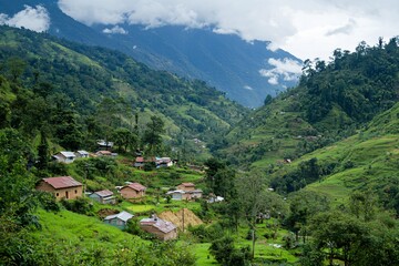 Scenic view of a lush green valley with village houses nestled among mountains under cloudy skies