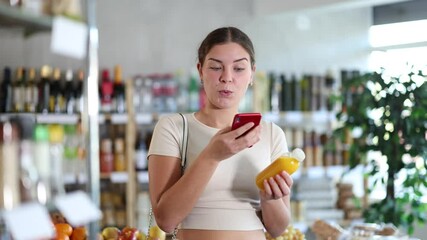 Young woman buyer scanning qr code for yellow smoothie in bottle in grocery store