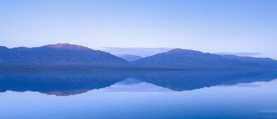 Fototapeta premium Soft blue clouds and mountains reflected in water at dawn. Made with generative AI