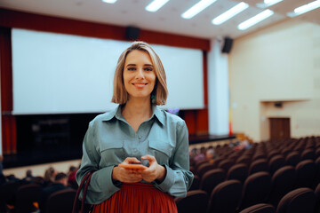 Happy Woman Holding her Phone in a Theatre Room . Cheerful event organizer texting in a conference...