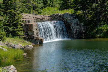 Serene waterfall cascading over rocky ledge into tranquil pond surrounded by lush greenery
