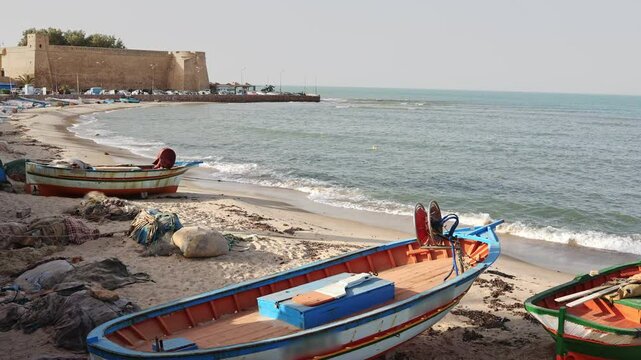 Ancient fortified citadel of Hammamet with formidable stone walls standing guard over tranquil Mediterranean seashore with old fishing boats of locals, Tunisia
