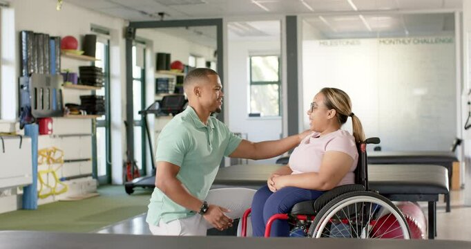 Encouraging woman with paraplegia in wheelchair, physical therapist during rehabilitation session