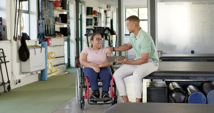 Rehabilitation center, therapist using tablet and supporting woman with paraplegia in wheelchair