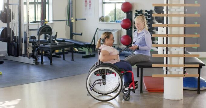 In rehabilitation center, woman with paraplegia in wheelchair exercising, resistance band, therapist
