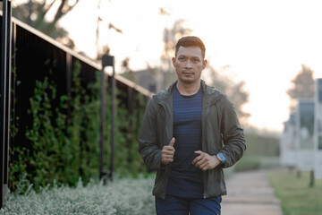 A male athlete enjoys a morning run in the park, smiling and exercising outdoors. Embracing fitness and happiness, he maintains a healthy lifestyle, feeling energized and positive in nature.