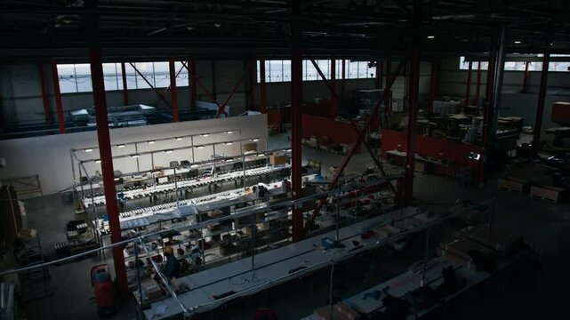 Wide no people shot of cavernous industrial lighting factory premises, several workshops with employees workplaces, electric tools and equipment, filmed by overhead surveillance camera at nighttime