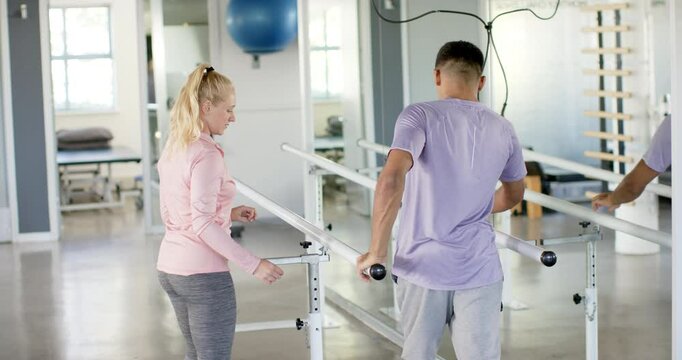 Man in rehabilitation using parallel bars with therapist in physical therapy center