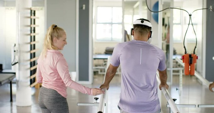 Man in prosthetic leg walking using VR headset with therapist on parallel bars