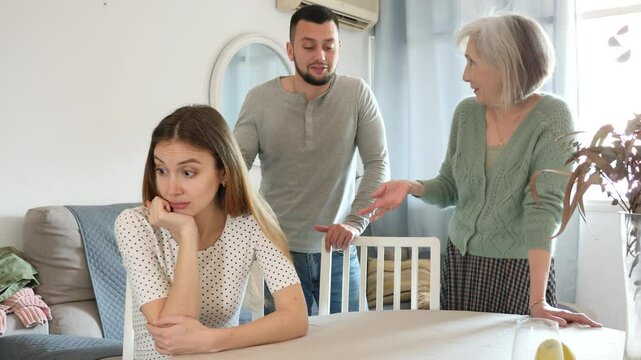 Stressed young woman sitting at home while her male and mature female relatives scolding her