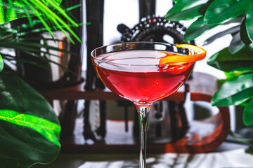 Hanky ​​Panky alcoholic cocktail drink with gin, vermouth, herbal liqueur and orange twist. White marble table with tropical leaves