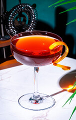 Rusty compass alcoholic cocktail drink with scotch whiskey, liqueur and orange twist. Green background, hard light and shadows