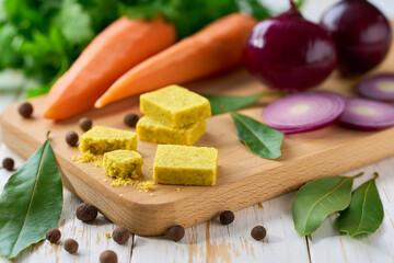 chicken bouillon cubes and fresh vegetables for soup on white wooden table, selective focus.
