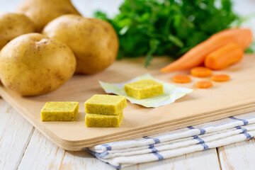 chicken bouillon cubes and fresh vegetables for soup on white wooden table, selective focus.