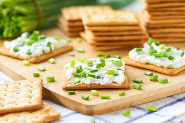 Salted biscuit with cheese cream with spring onions on a wooden table.
