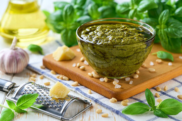 Traditional italian sauce pesto in a bowl with basil leaves on a light kitchen table table.