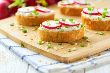 Cutting baguette with soft cream cheese and radish on a light kitchen table. Tasty summer snacks.