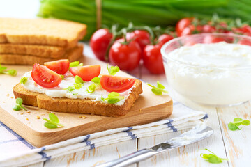 Sandwiches or toast with tomatoes cherry, cream cheese, olive oil and microgreen on a plate on white table.