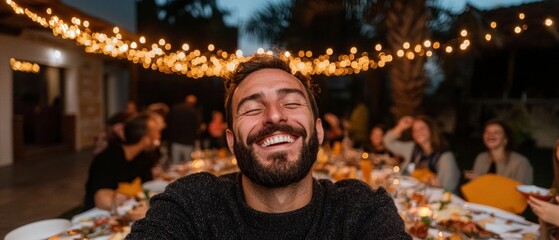 Obraz premium Happy Man at Festive Outdoor Dinner Party with String Lights