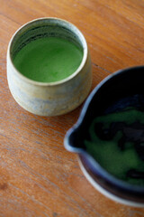 Cup of fresh matcha tea, green tea and empty bowl, on wooden table.