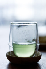 Cup of hot green tea on wooden table. Glass cup backlit.