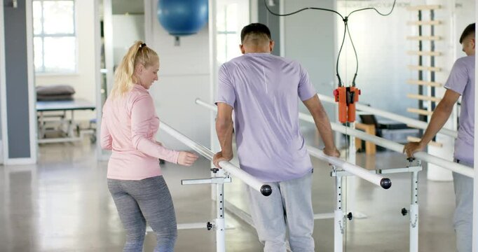 Assisting with leg exercises, man supports another man using parallel bars in rehab gym