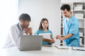 Two male doctors and a female nurse meet at a table in the hospital, collaborating on medical tasks, using laptops and computers, showcasing teamwork,and focusing on health,medicine,and patient care