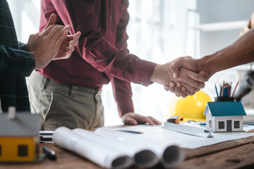 Two male engineers and a strong woman discuss blueprints and home design at a table. They work as a...