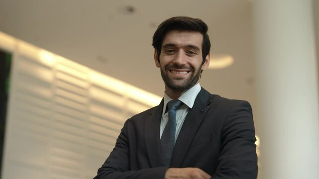 Professional business man turn around while standing with arm folded. Happy caucasian investor looking at camera with confident while crossing arm at hall with blurring background. Portrait. Exultant.