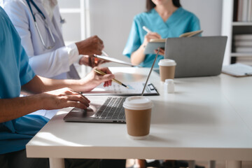 Two male doctors and a female nurse meet at a table in the hospital, collaborating on medical tasks, using laptops and computers, showcasing teamwork,and focusing on health,medicine,and patient care