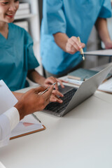 Two male doctors and a female nurse meet at a table in the hospital, collaborating on medical tasks, using laptops and computers, showcasing teamwork,and focusing on health,medicine,and patient care