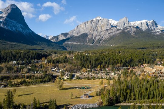 Panoramic view of Canmore mountain town nestled in a valley. Houses and a playground are visible amidst the trees. A beautiful autumn day, Alberta, Canada
