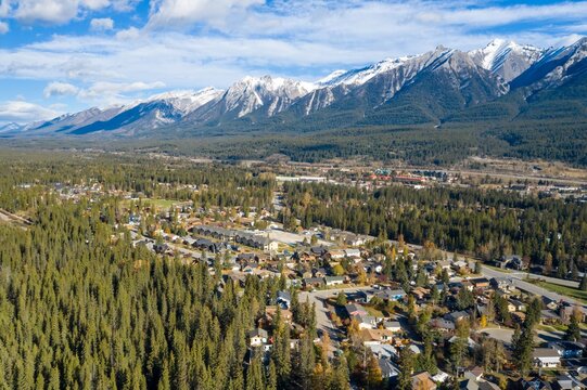 Aerial view of Canmore mountain town nestled in a valley. Homes and businesses are surrounded by evergreen forests, with snow-capped peaks in the background.  Alberta, Canada